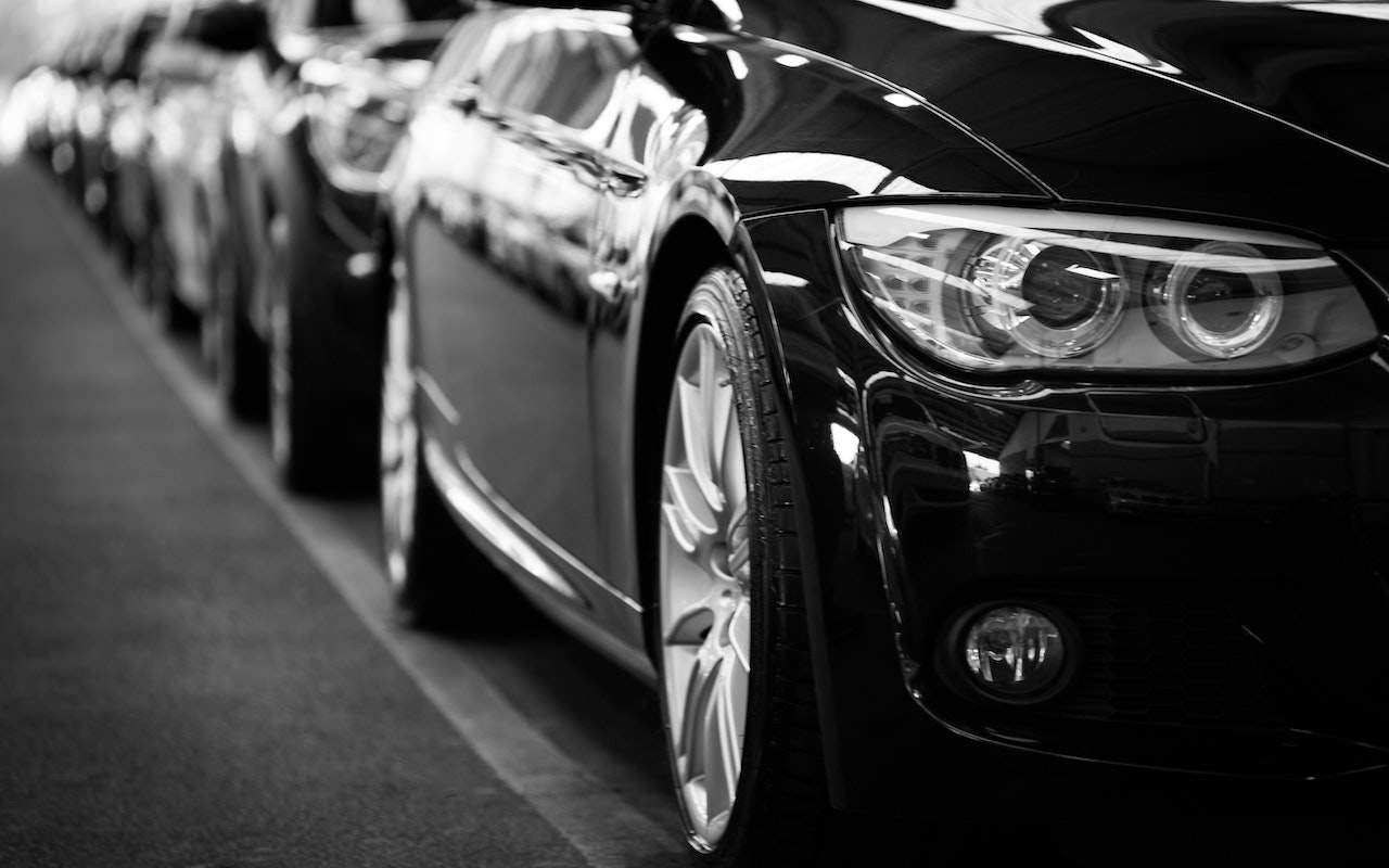 A close-up, black-and-white photo of several sleek cars parked in a row, focusing on the front wheel and headlight of the nearest vehicle—perfect for The Ultimate Guide to Corporate Transportation in Paris.