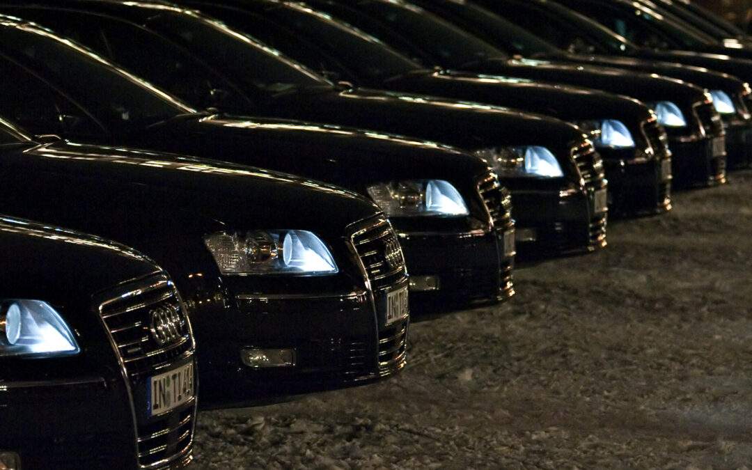 A row of black cars with headlights on, parked closely side by side at night on a snowy surface—evoking the elegance you'd expect when learning how to choose the best Limousine service in Paris for your next business trip.
